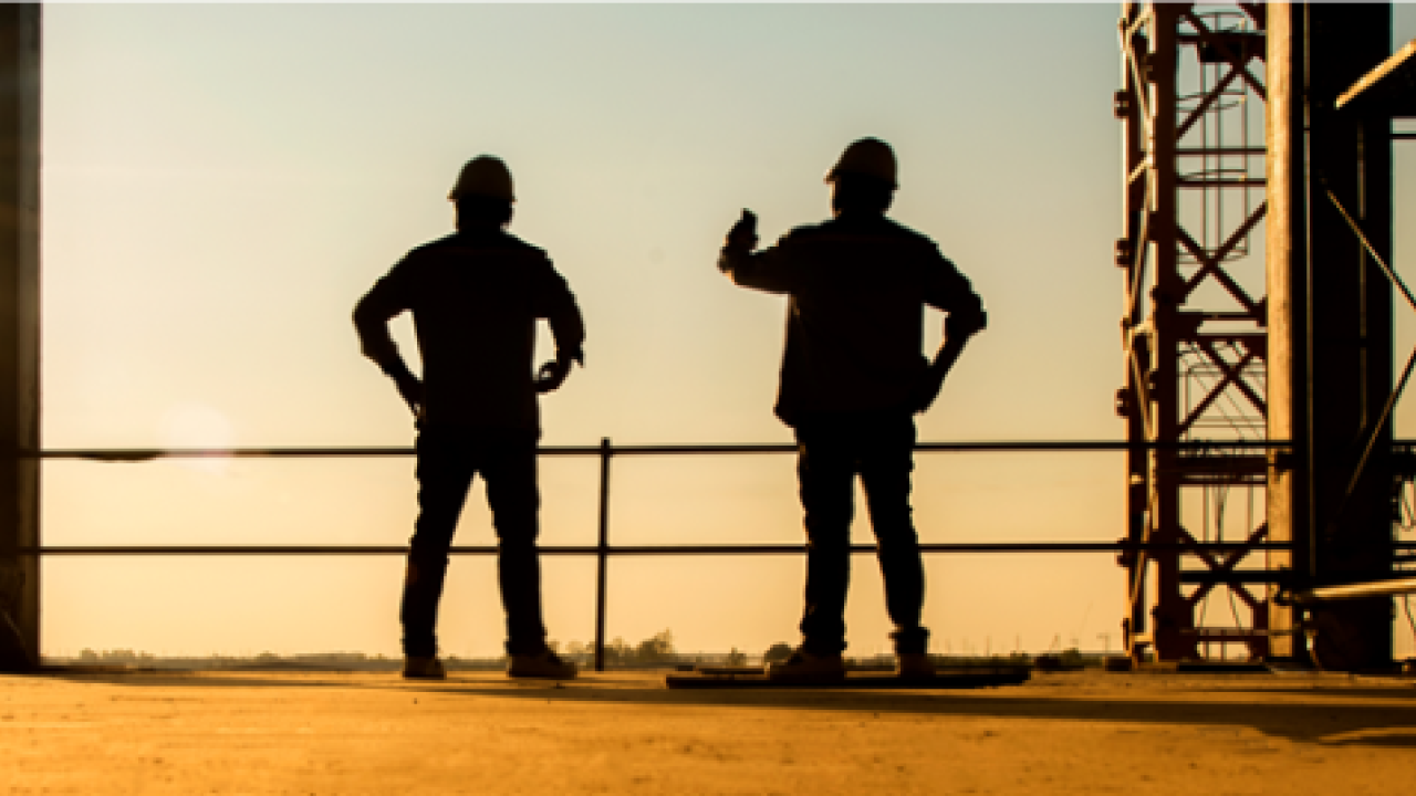 silhouette of two workers with hard hats at a worksite