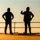 silhouette of two workers with hard hats at a worksite